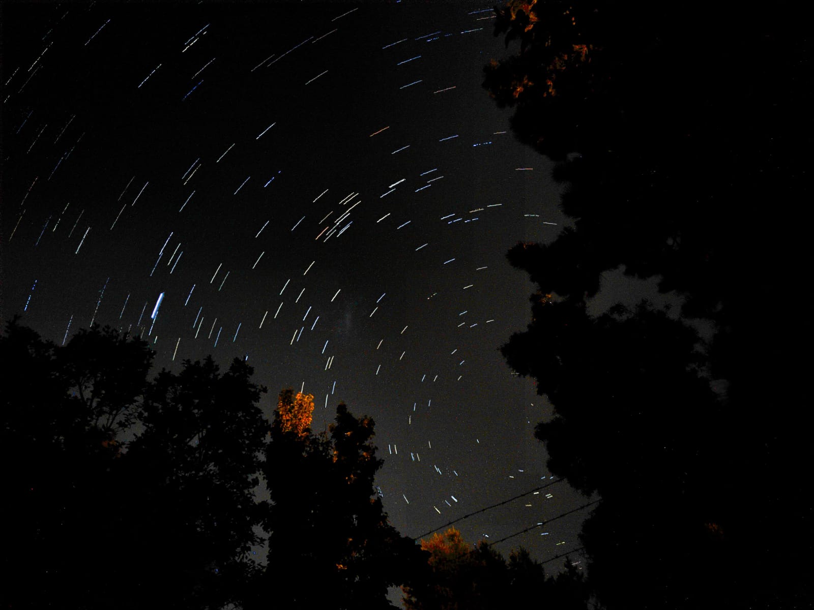 Night sky with circular star trails over a dark landscape